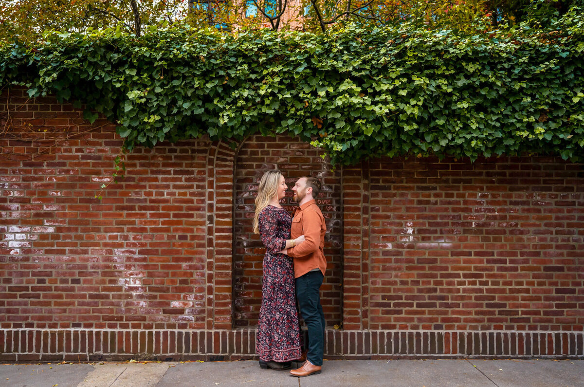 Man and woman, hugging in front of the brick wall that has the word love written on it in New York City