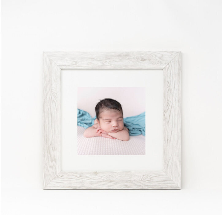 A wooden framed photo of a newborn baby hanging on a wall
