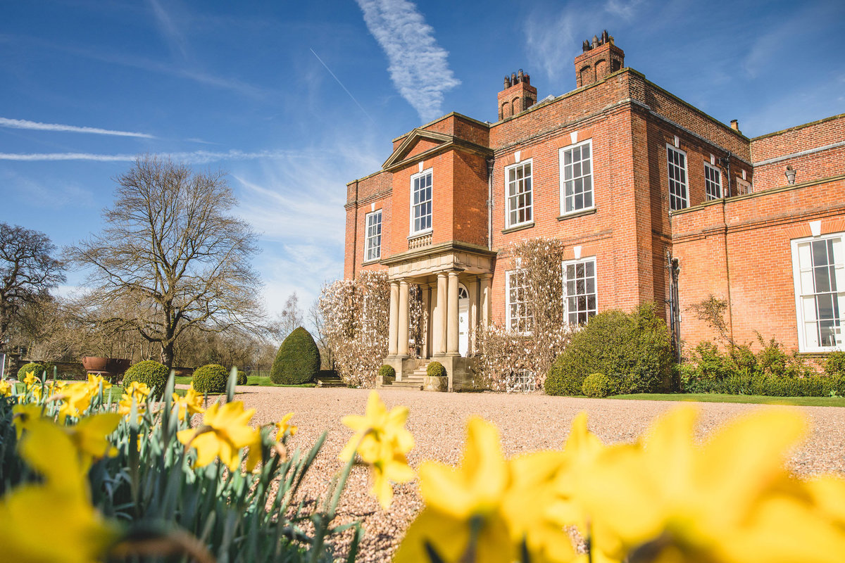 A photograph of Iscoyd Park from the front of the house taken with daffodils in the foreground and a blue sky in summer