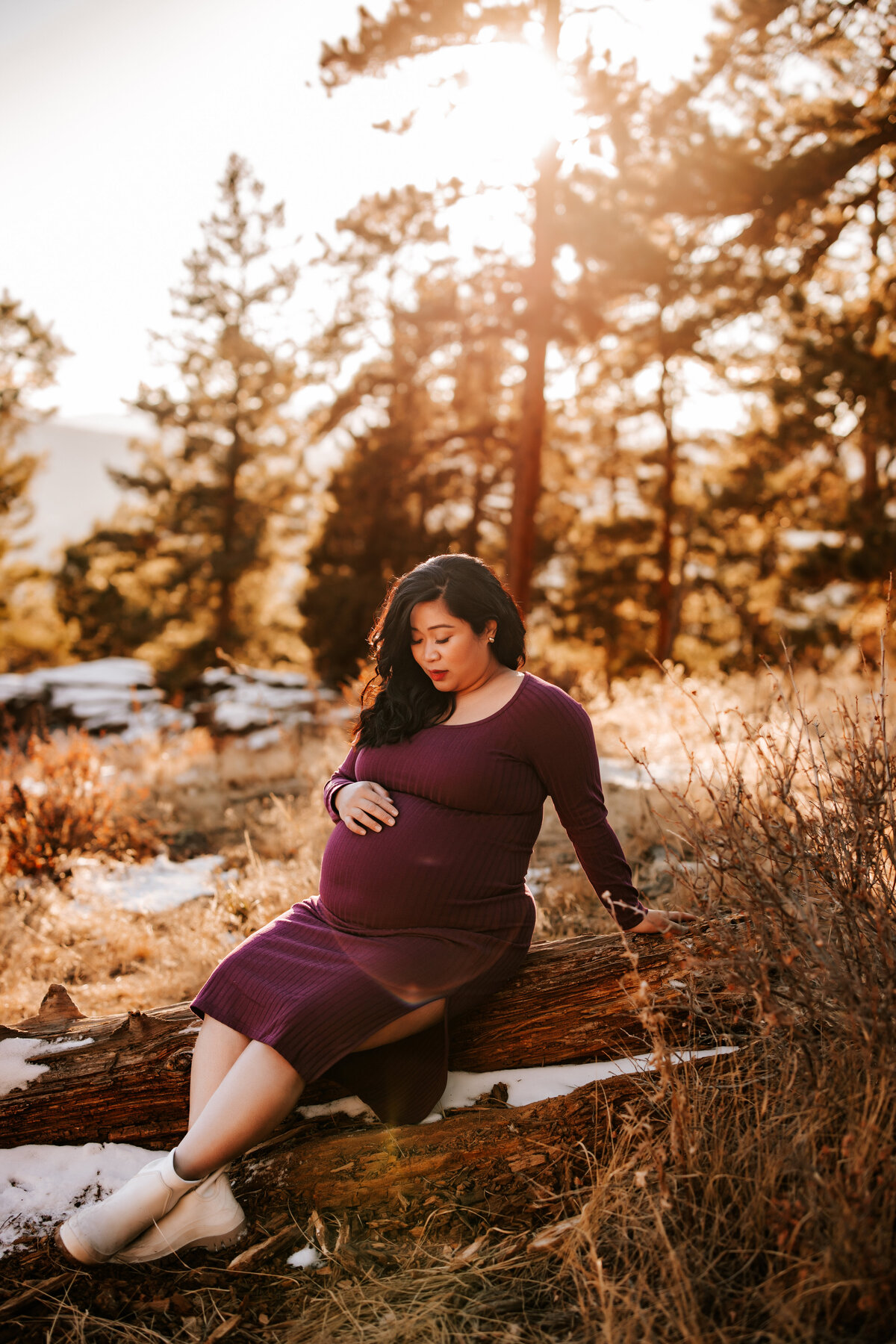 pregnant mom wears a tight purple dress on tops of snowy rock in the mountains in denver colorado