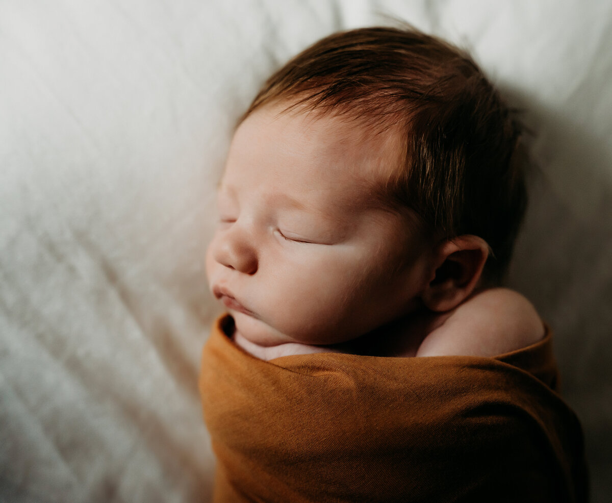 Newborn Photographer,  a baby sleeps swaddled in blankets