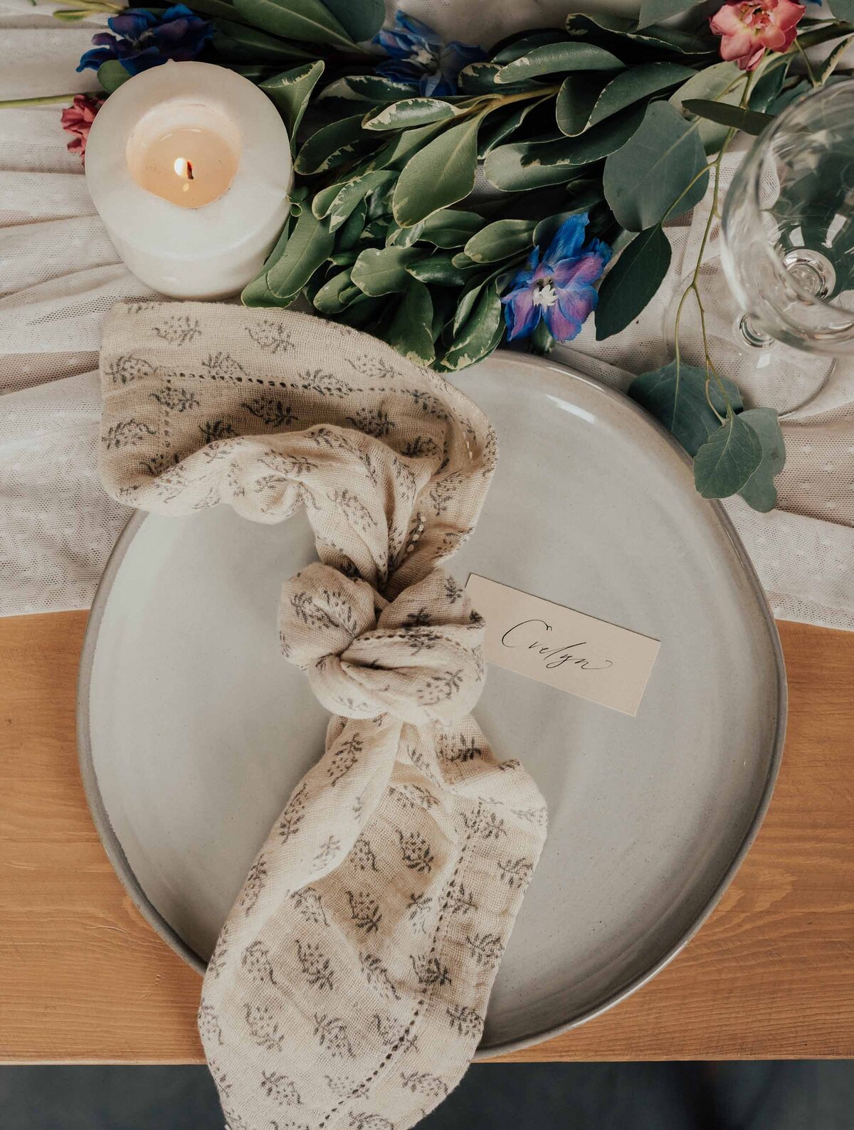 Maddie Rae Photography plate setting. the cloth napkin tied in a knot, there are candles and flowers on the table above the plate
