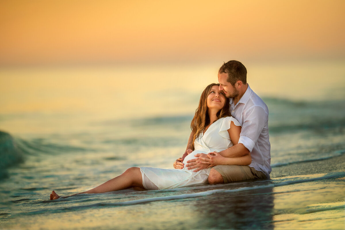 Parents holding baby bump  while sitting in the water of gulf of Mexico  beach in Florida