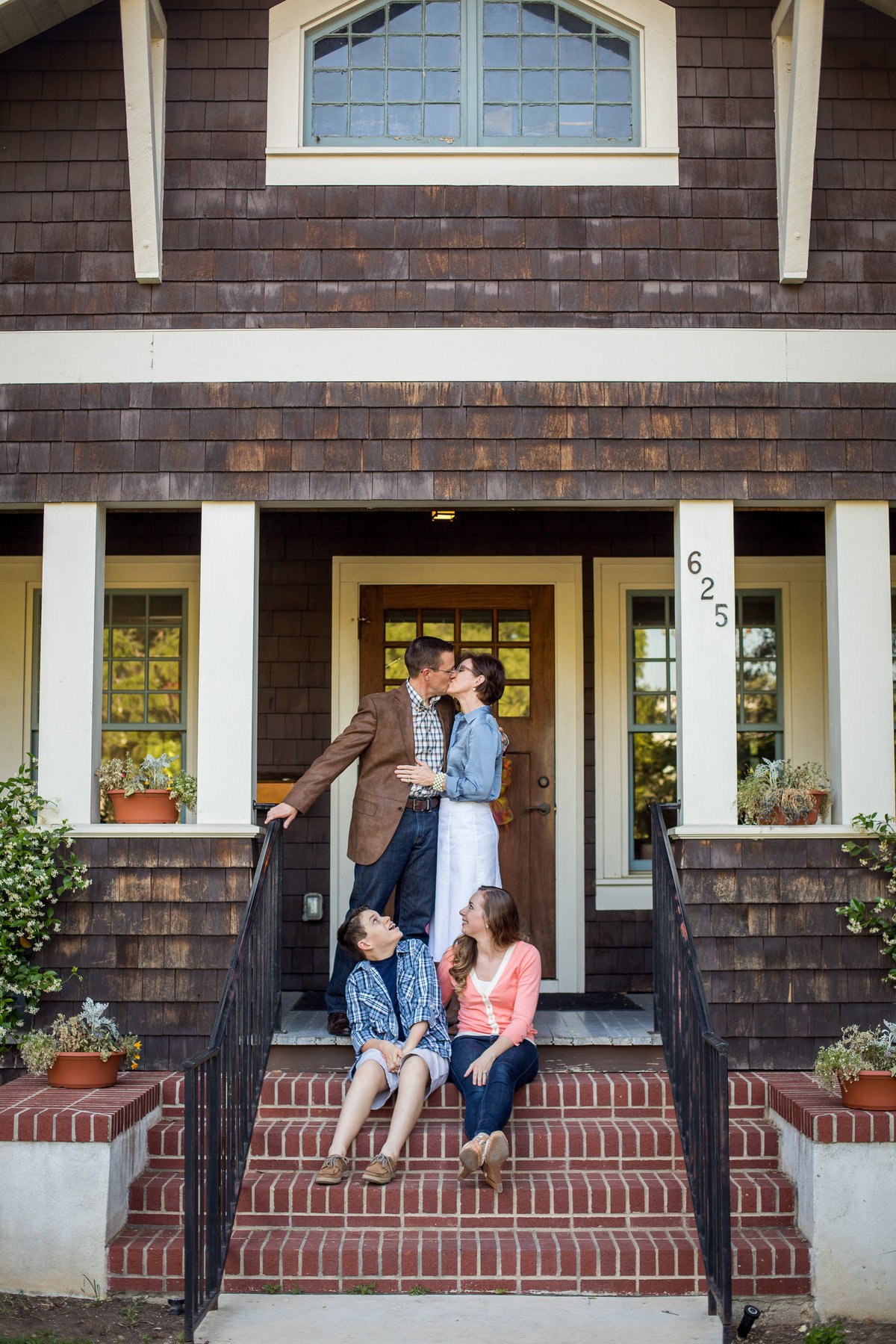 family portrait photography of mom and dad kissing on front porch and kids looking by San Antonio Photographer Expose The Heart