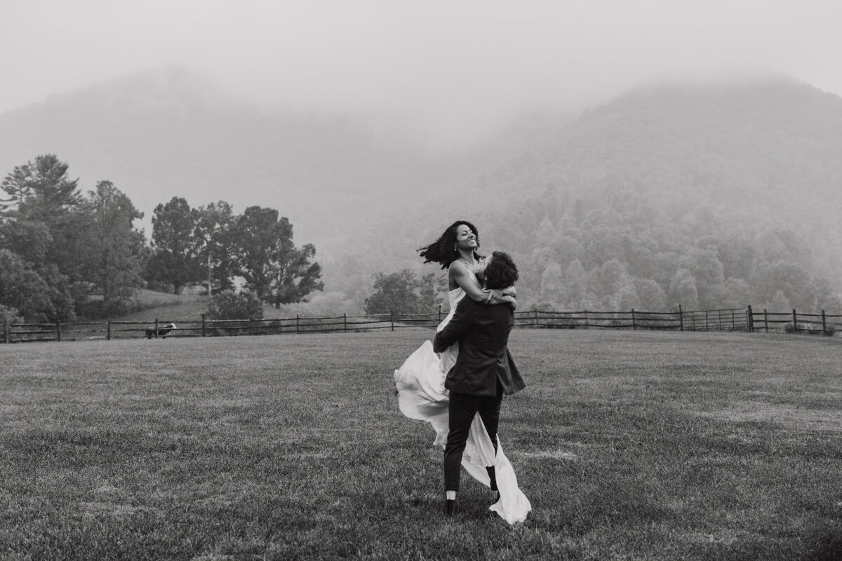 Groom holding bride as they spin around in a field. photo is black and white.Adventure Awaits: Celebrate Love in the Great Outdoors