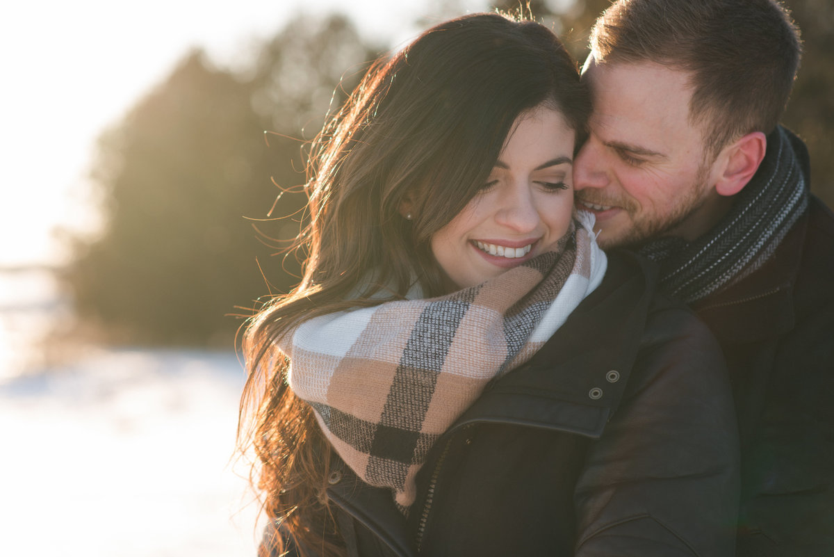 Engaged couple cuddling at sunset in winter