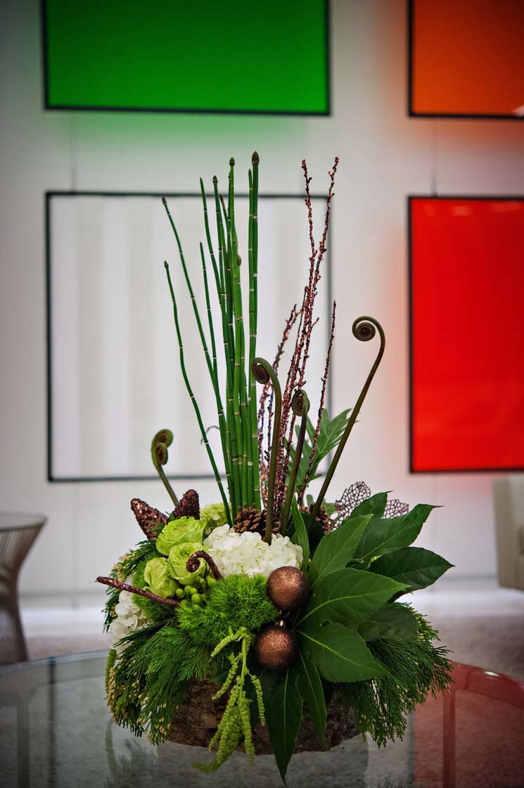 winter arrangement of green hydrangea, green roses, fiddlehead fern, equisetum, brown ornaments, in barked vase with trailing green amaranthus