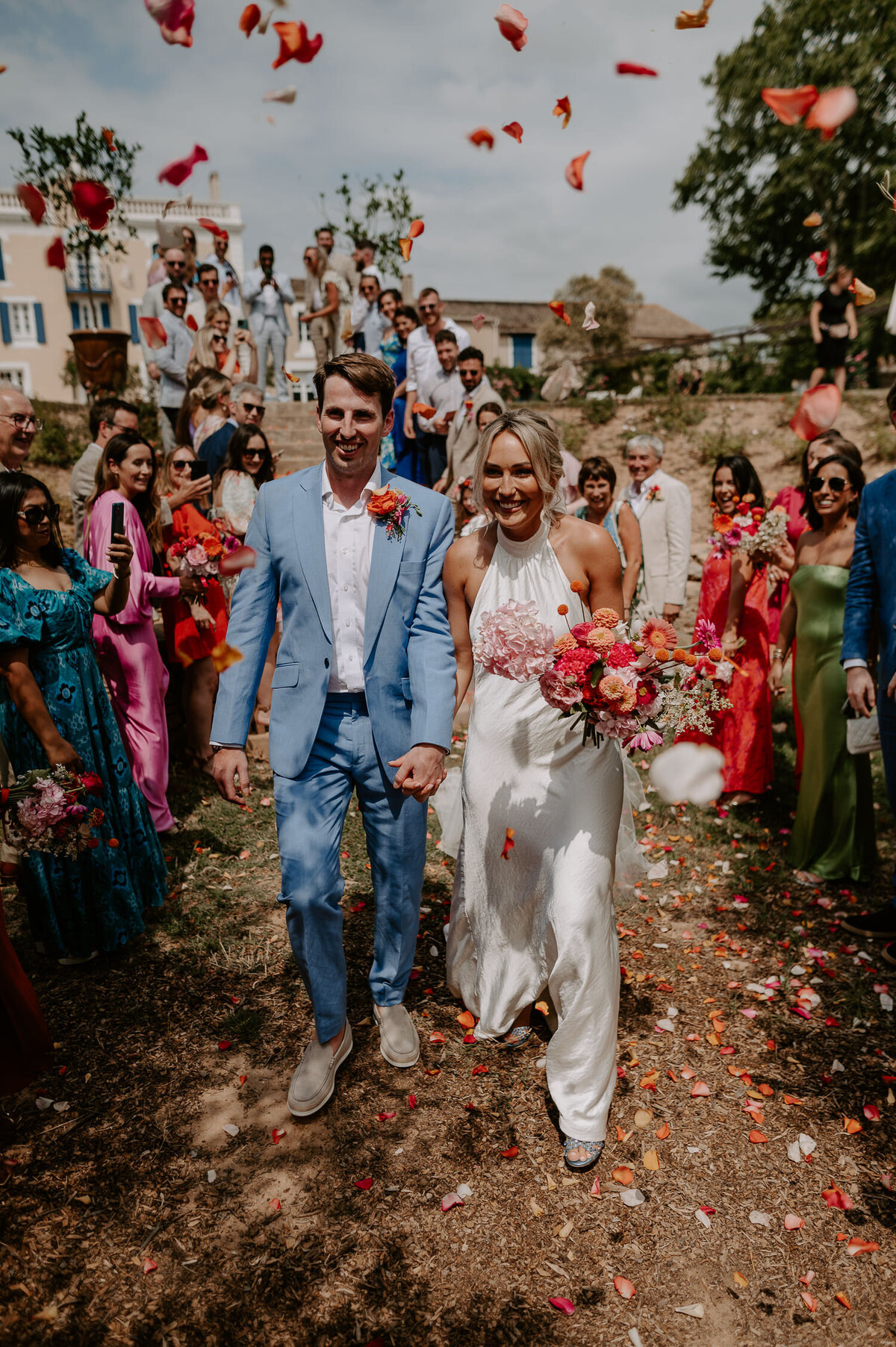 A bride and groom walk down the steps of Chateau Canet to a huge natural petal confetti tunnel.