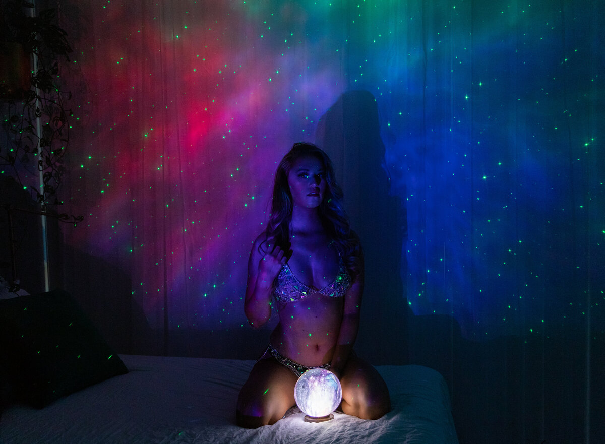 A galaxy lamp was used to project the multi colored background. Woman is sitting on the bed and holding a small light up moon lamp