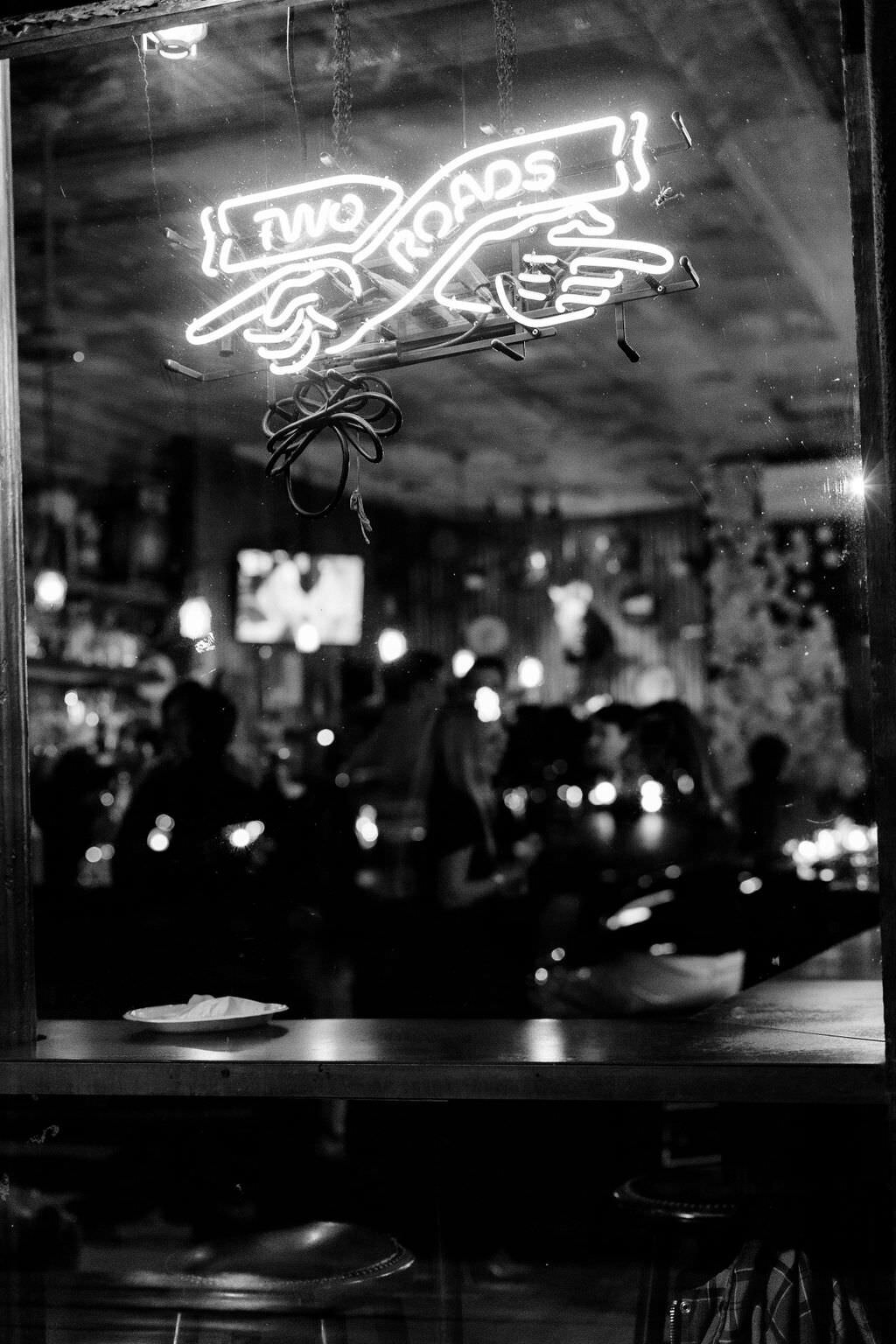 black and white photo of a neon sign in a bar window that says two roads