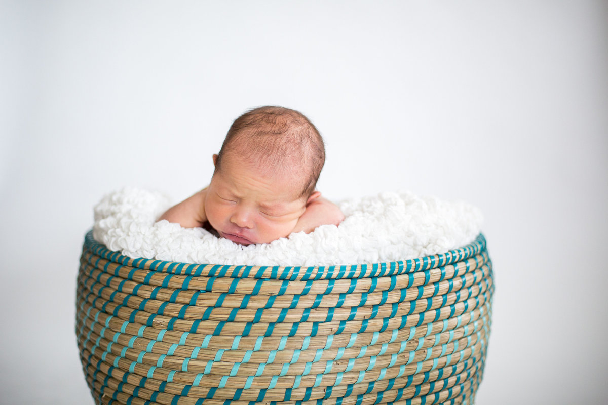 Newborn photography of infant laying in basket filled with white blanket.