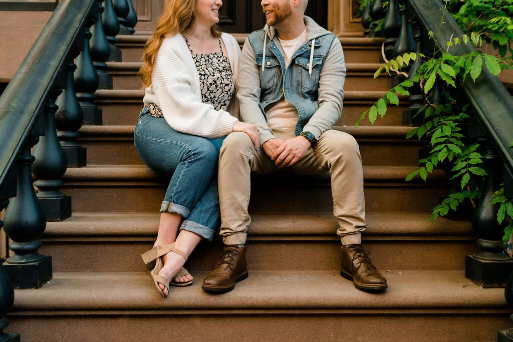 woman with her arms on a man's leg as they sit on stairs and smile at each other