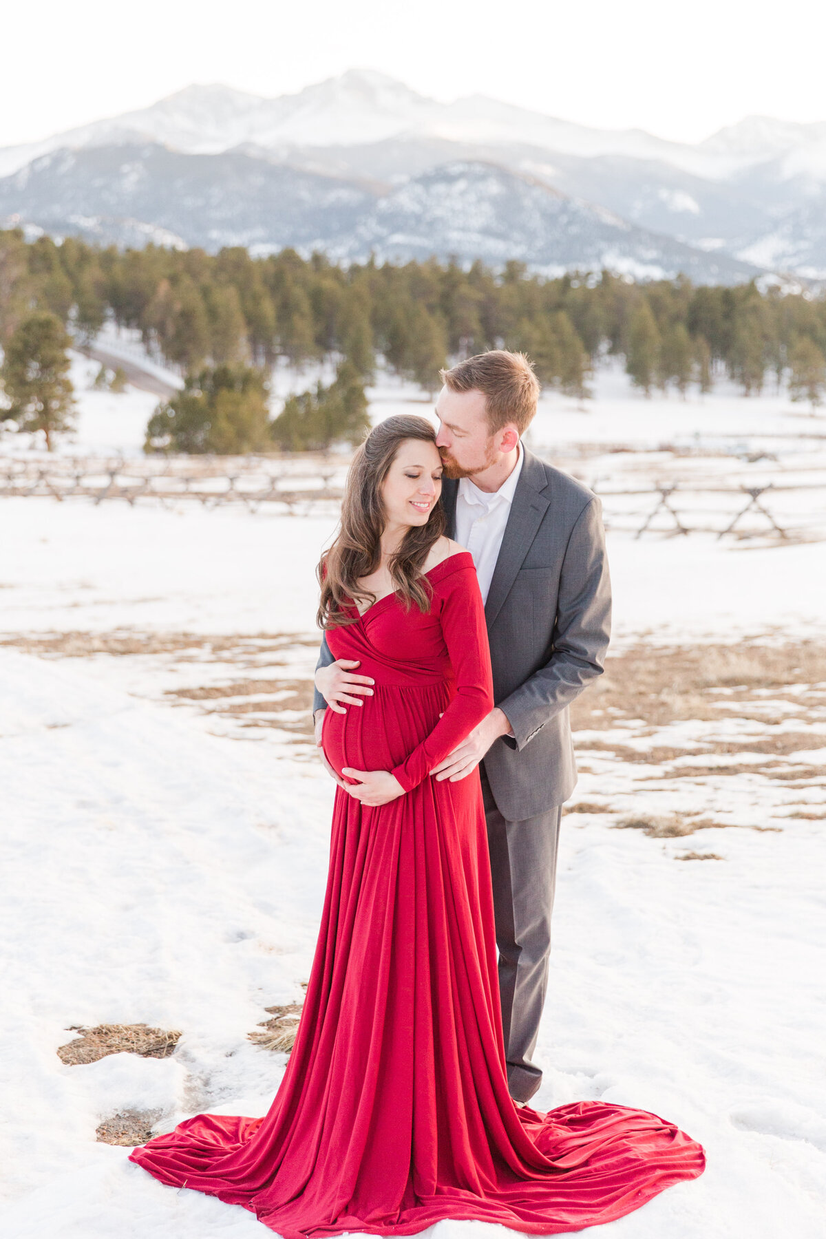 Red dress maternity session husband kisses wife's forehead Estes Park, Colorado