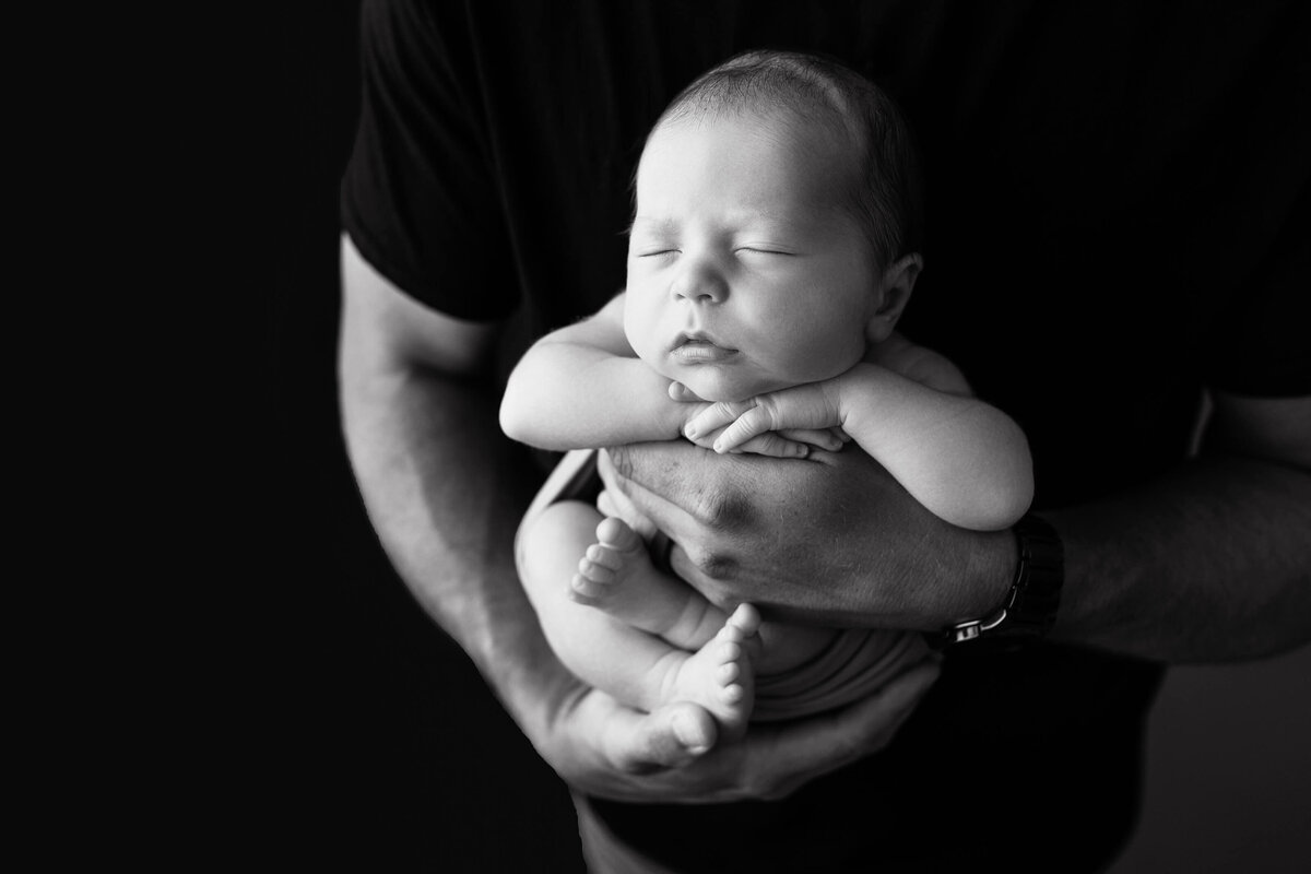 black and white image of newborn baby being held by dad