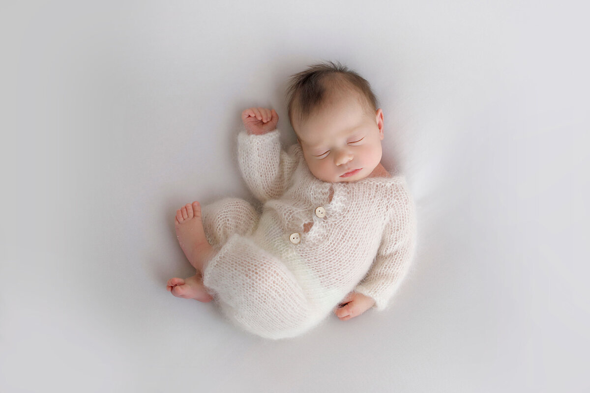 baby-in-a-white-romper-all-curled-up-for-her-baby-shoot