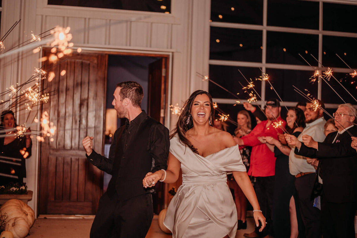 Photo of a bride and groom celebrating as they run through a tunnel of sparklers