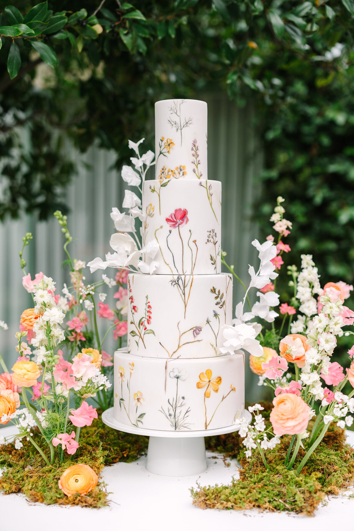 four tier wedding cake decorated with flowers and surrounded by soft pastel florals.