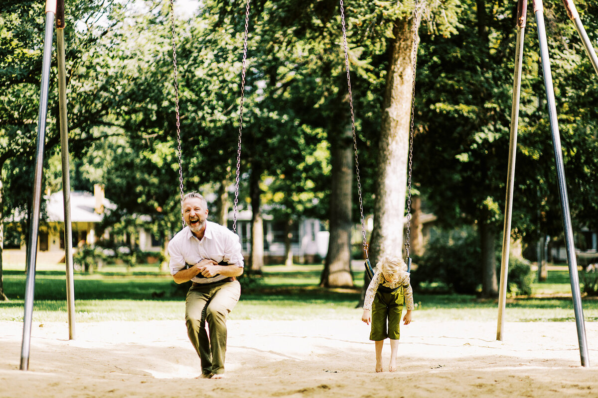 a dad and daughter swing and laugh during family photo session
