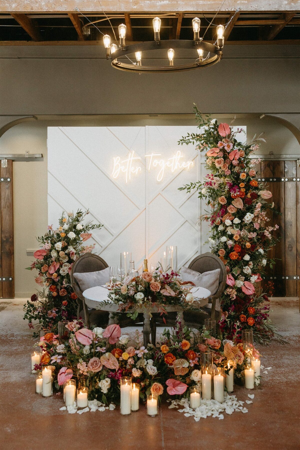 White ceremony backdrop surrounded by colorful florals in crimson, pink and white with candles