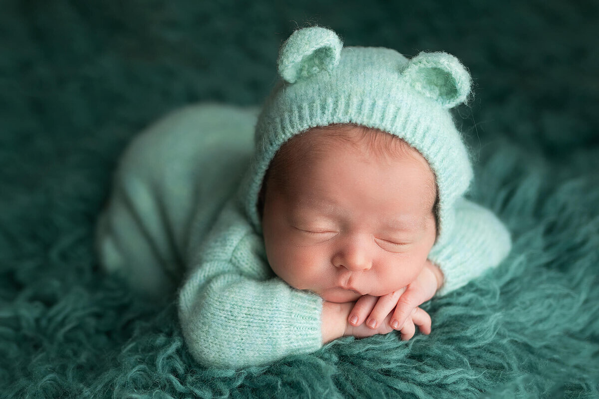 Newborn Boy wearing a blue bear romper and bonnet.
