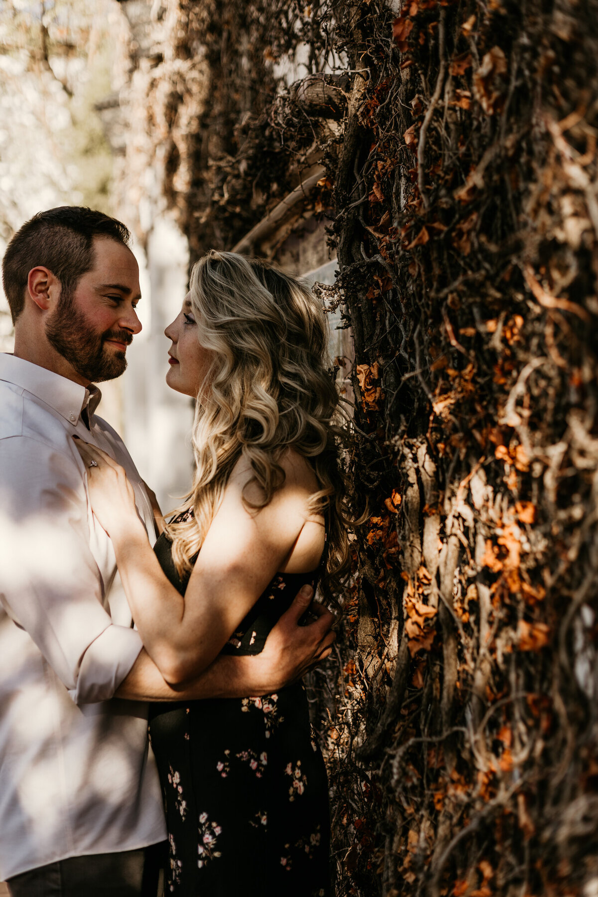 engaged couple leaning on a white wall with vines