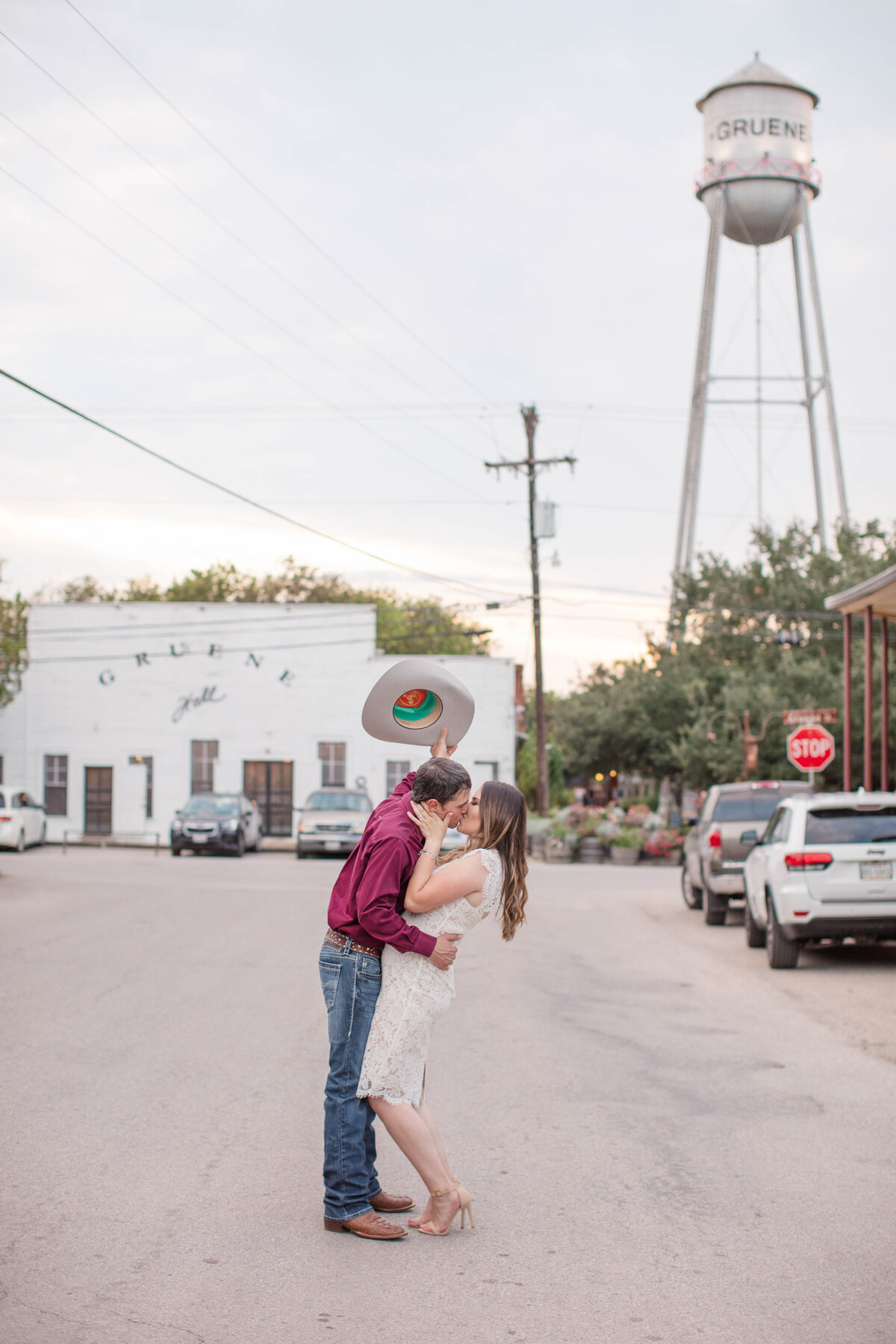 engagement portrait big kiss with cowboy hat in street of Gruene Hall with water tower by New Braunfels wedding photographer Firefly Photography