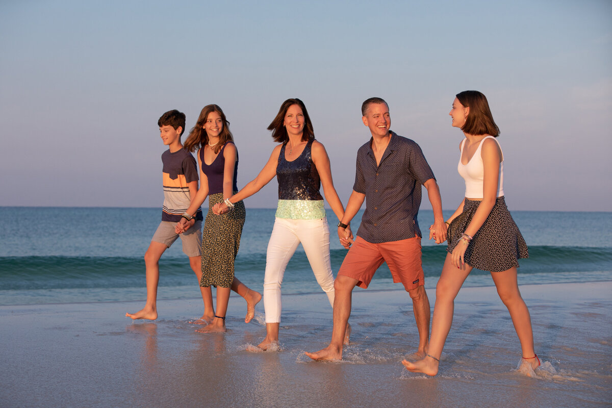 A family holding hands and walking along the small waves at the beach