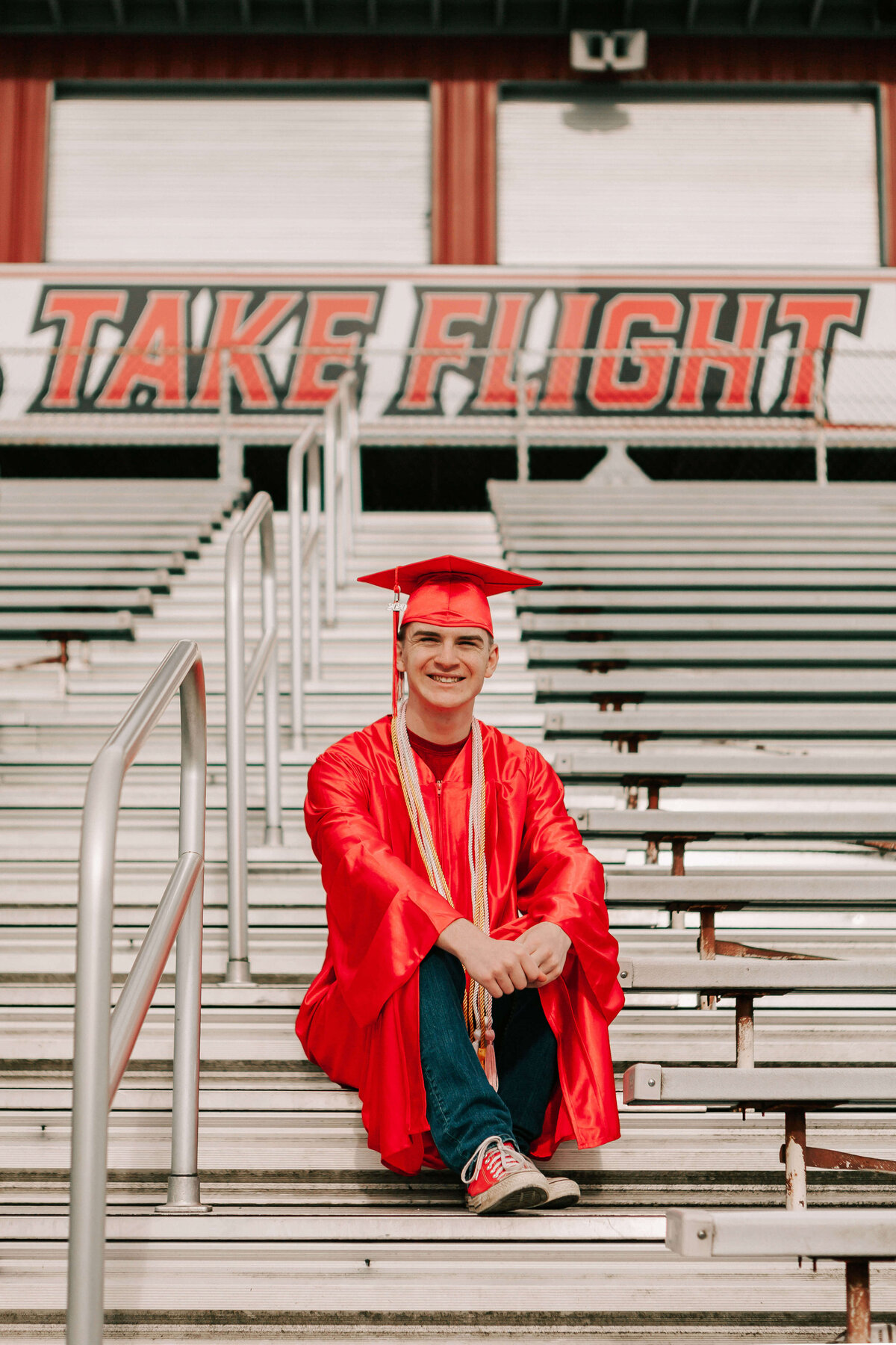 A high school senior in a red cap and gown sits on the bleachers at South Albany High School
