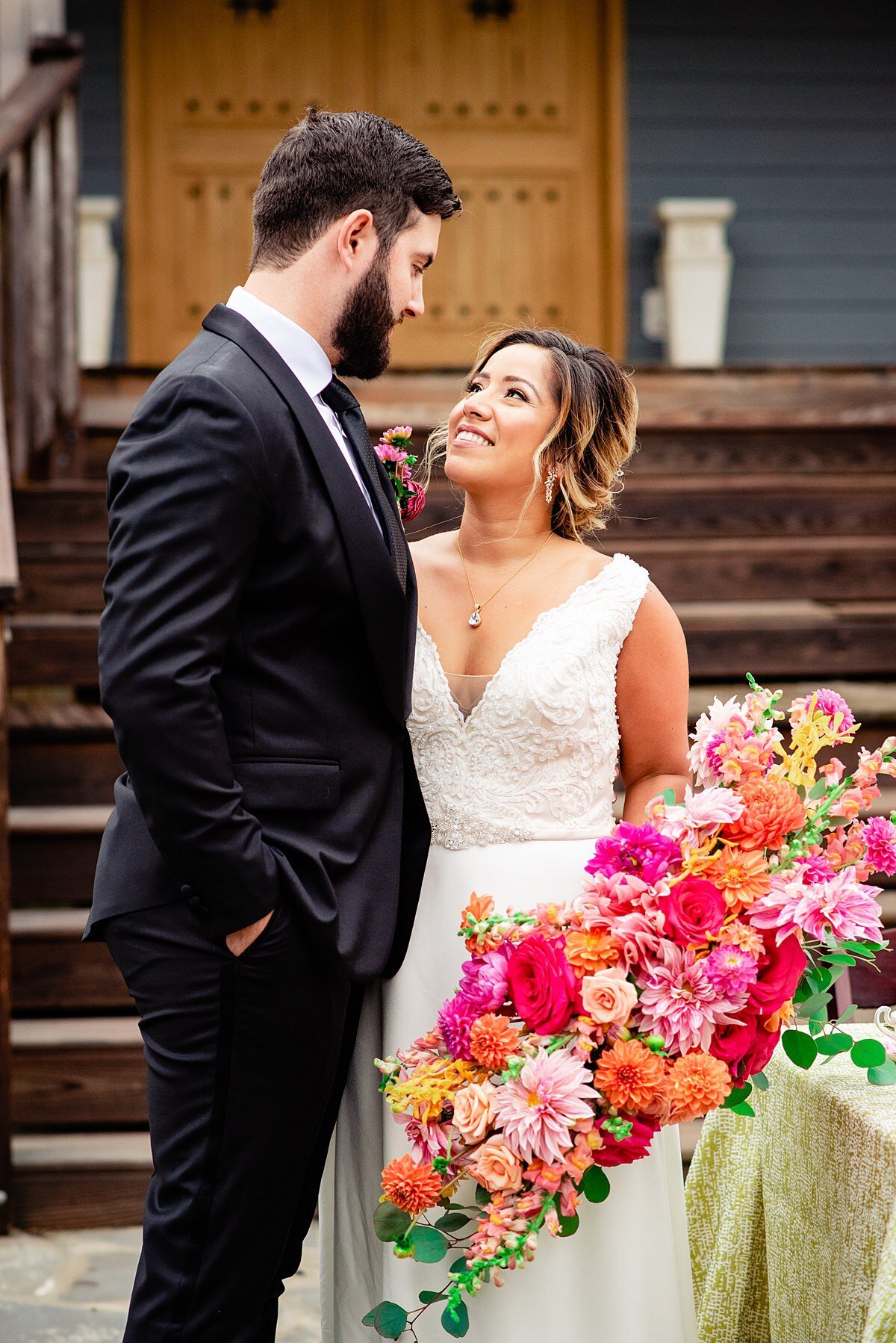 Couple standing together, she has a large horizontal pink red and orange wedding bouquet