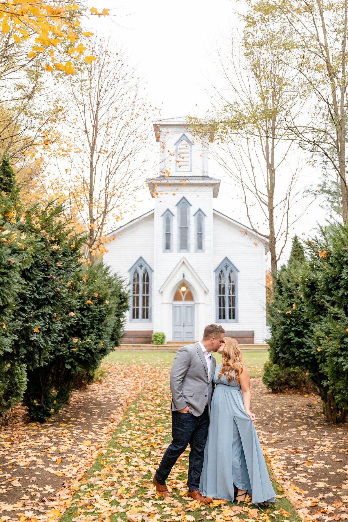Guy-kisses-his-fiance-in-front-of-the-Cranberry-Creek-Gardens-Chapel-during-their-fall-engagement-session