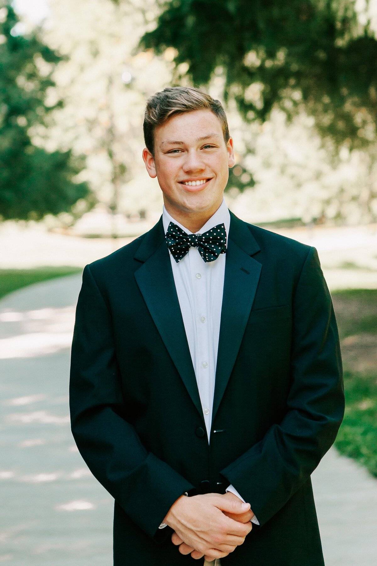 A high school senior boy stands in a black tux smiling
