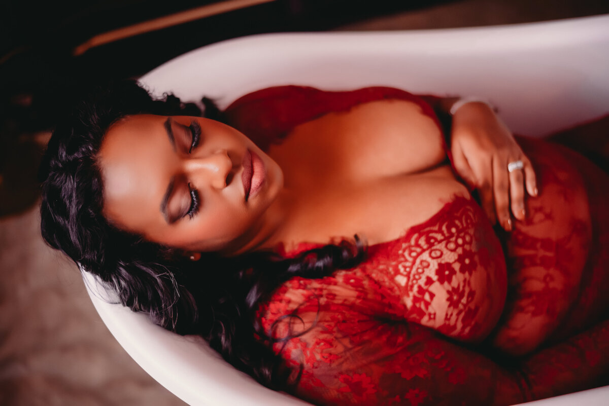 woman in dry bath tub holding her belly in red dress