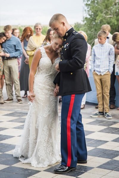 A bride and groom, who is dressed in a military uniform, bow their heads for a prayer before their reception dinner.