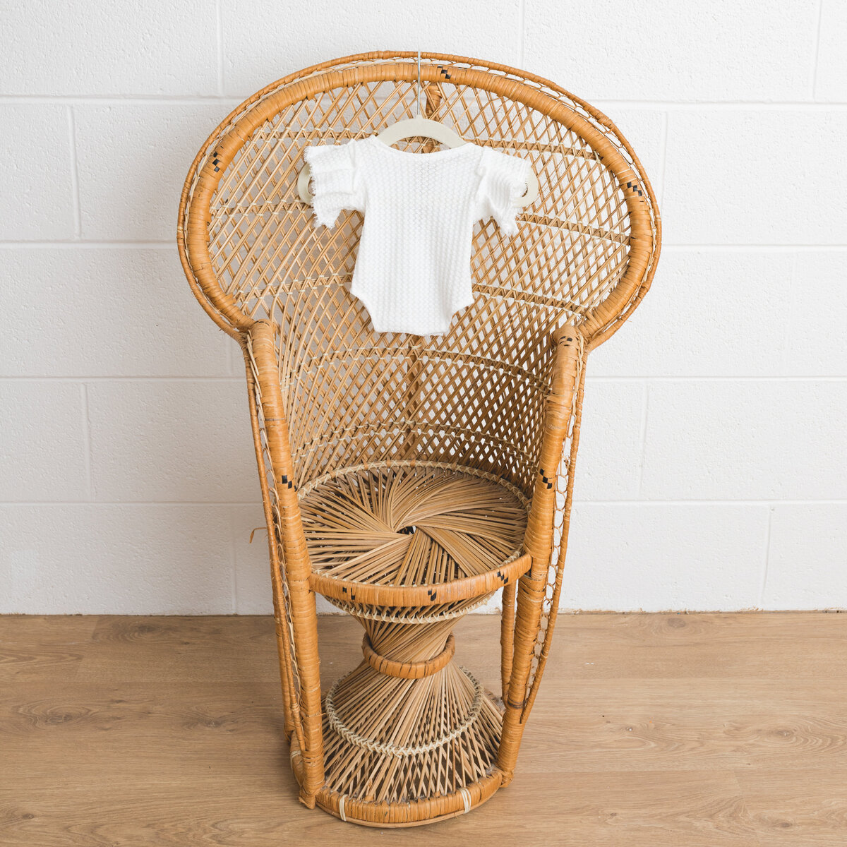 Image depicts a miniature peacock chair in a photography studio on the chair hangs a tiny newborn outfit in white knit  with l a lace bodice.  This image is a sample of Lauren Vanier Photography's newborn client wardrobe. Image taken in Hobart Tasmania