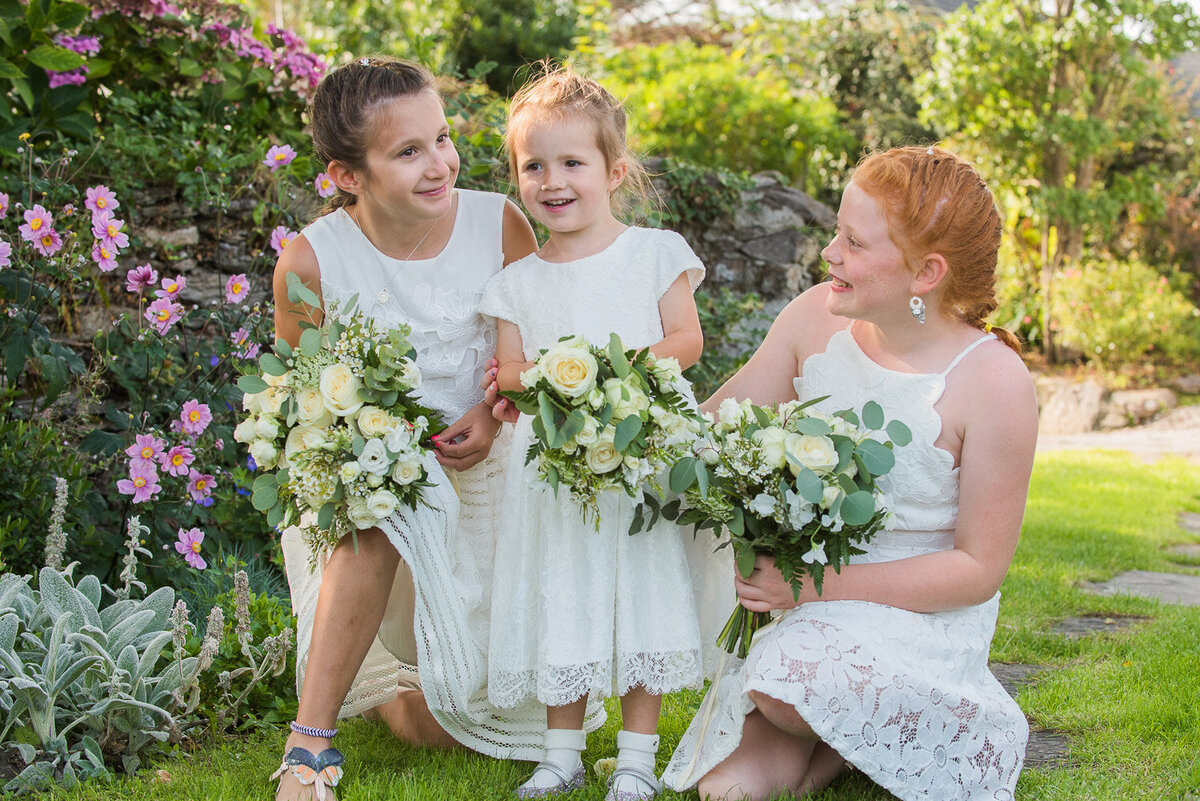 three flower girls holding white wedding bouquets in a floral garden laughing