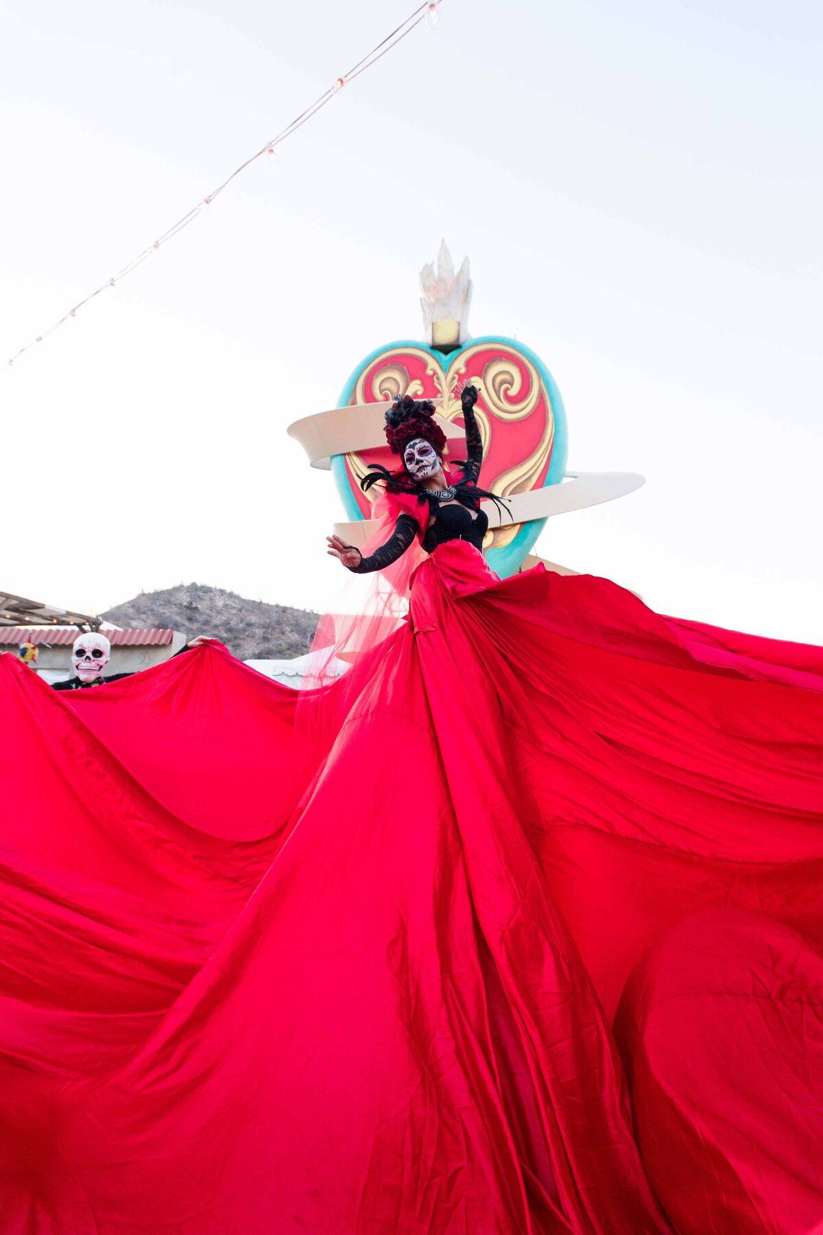 A women on stilts dances wearing long red dress for an immersive offsite celebration.