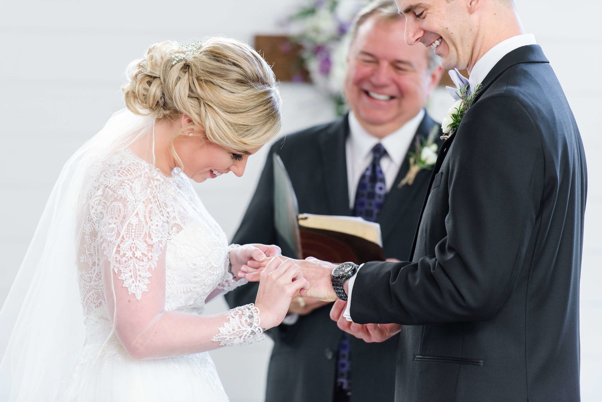 Bride and groom laughing together as she puts his wedding ring on his finger during their Cross Creek Wedding ceremony