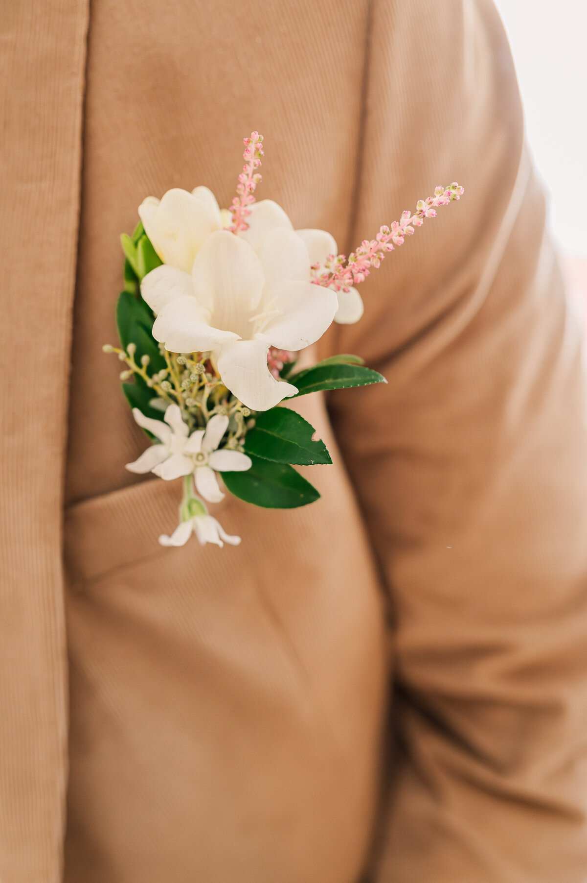 A detail shot of spring flowers in a boutineer on a brown suite coat by JoLynn Photography
