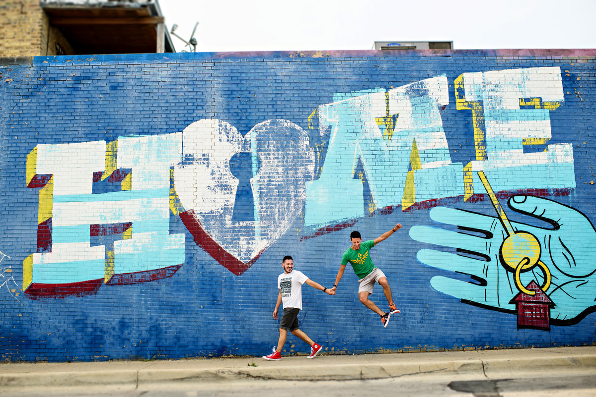 Two grooms jump for joy in front of a graffiti mural in Chicago.