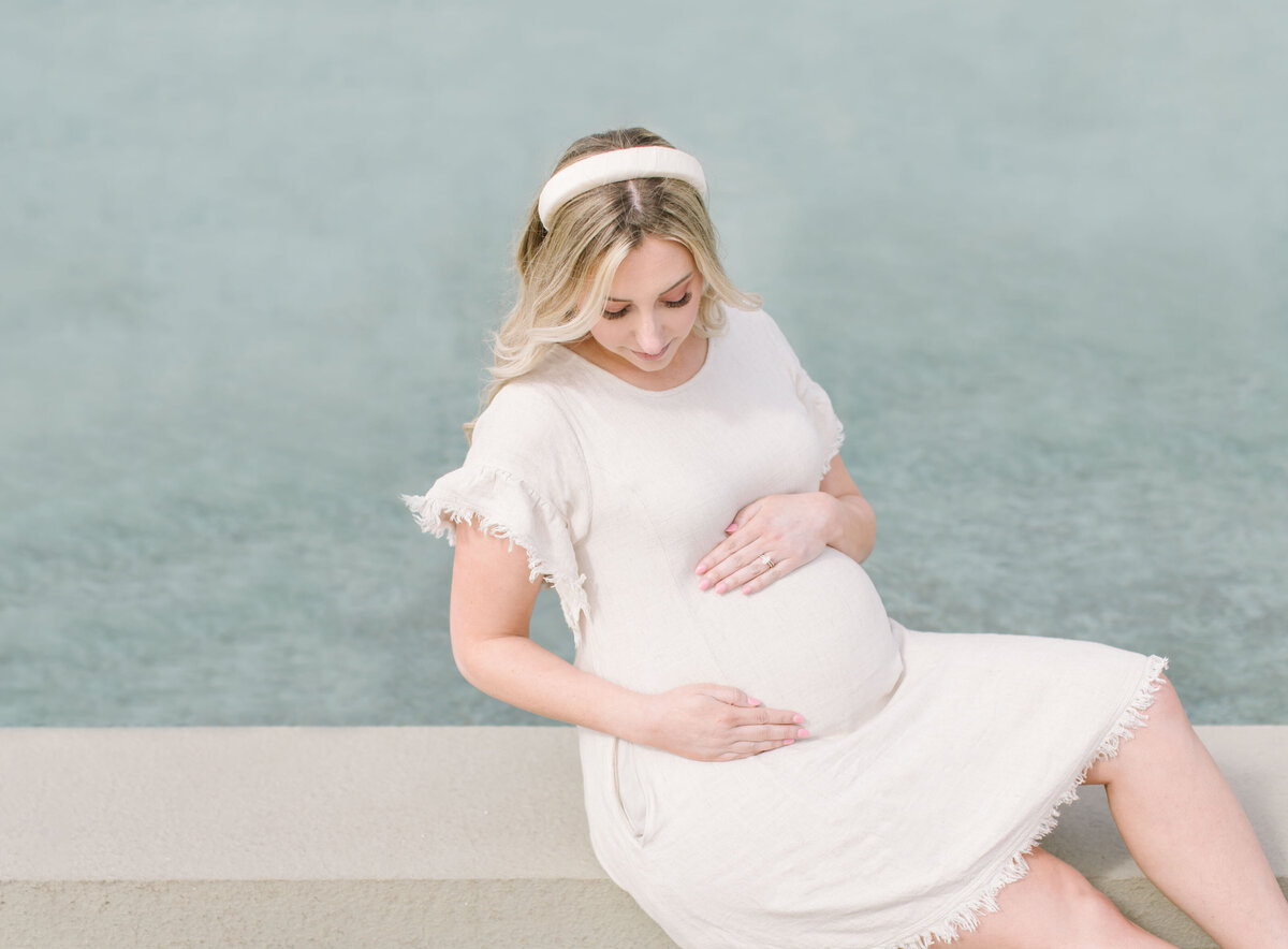 Maternity photo of mother sitting beside fountain gazing down at bump