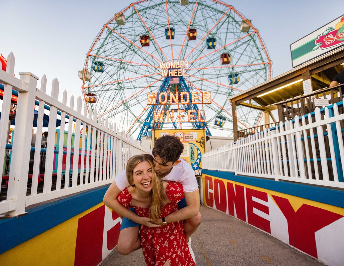 A person holding their partner on their back in front of a ferris wheel.