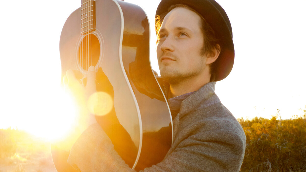 Country Music Artist Portrait Del Barber with guitar holding guitar straight up in the air with sun setting behind him