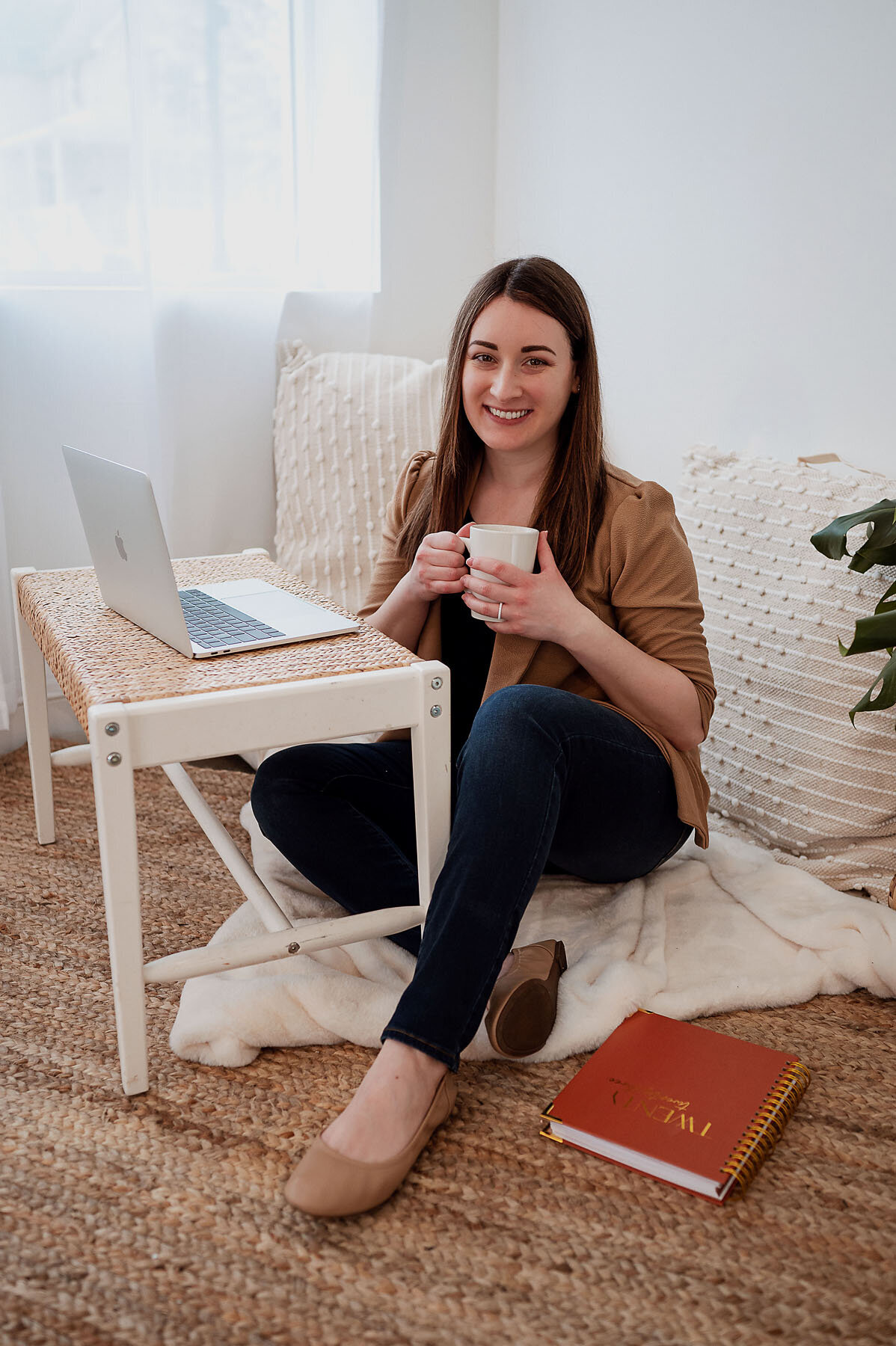 Creative business owner sitting on floor of studio with laptop and drinking a cup of coffee