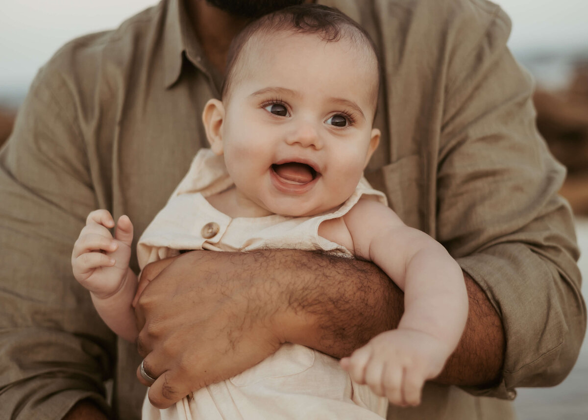 A close up photograph of a gorgeous baby smiling in his dad's arms.