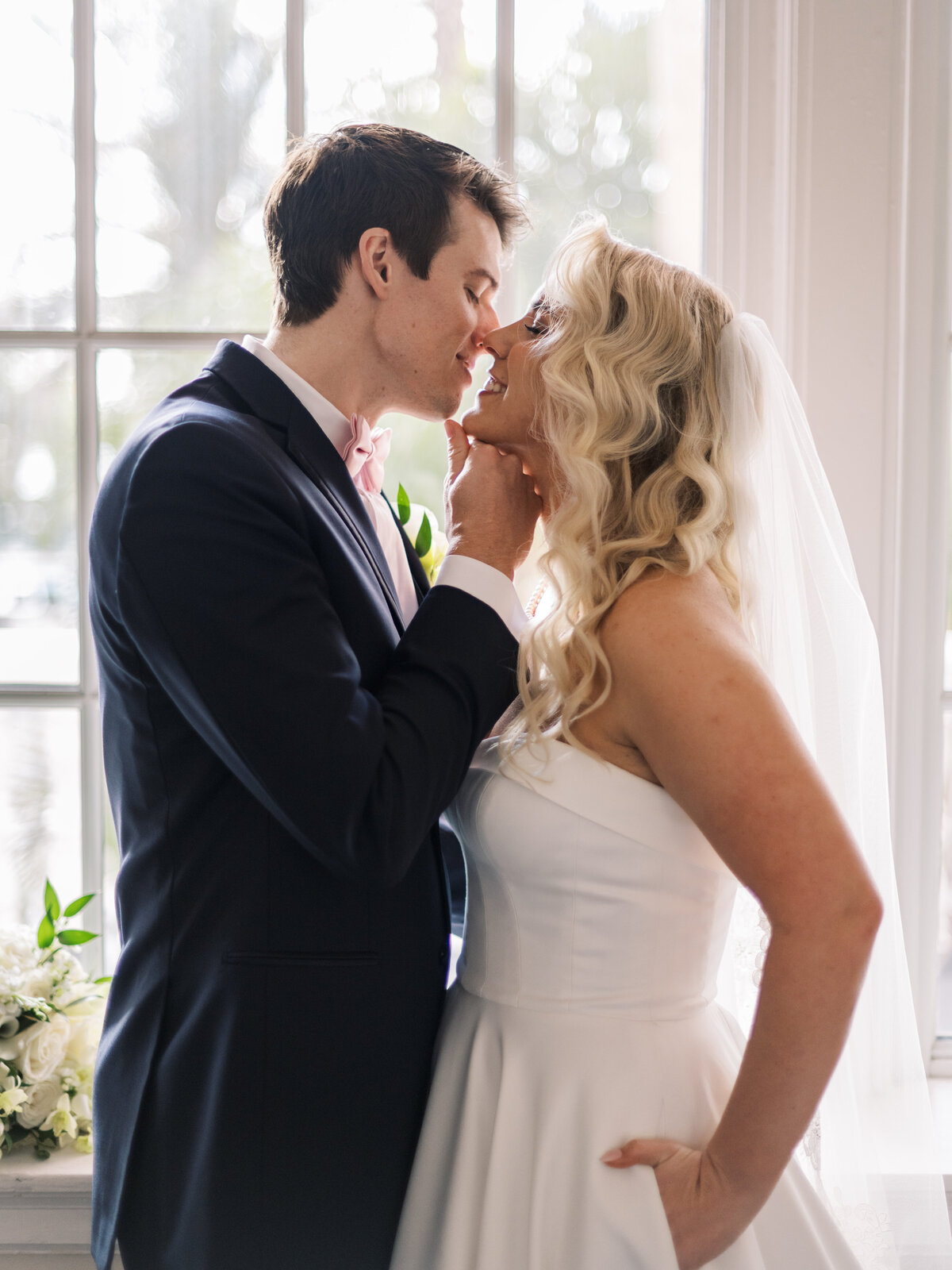 bride and groom kissing by a window
