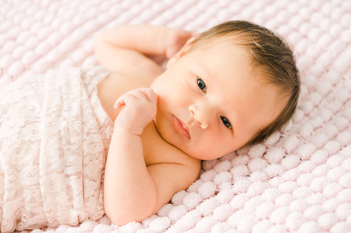 An Edmonton newborn baby girl wrapped in pink laying on a pink blanket.