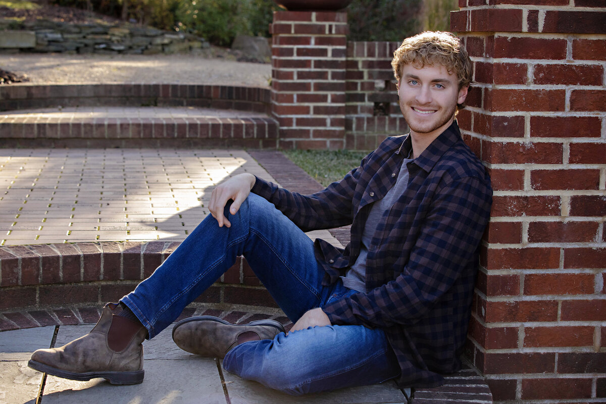 Polished autumn portrait of college senior seated on brick terrace steps framed by colorful leaves at UNCC Botanical Garden Charlotte NC