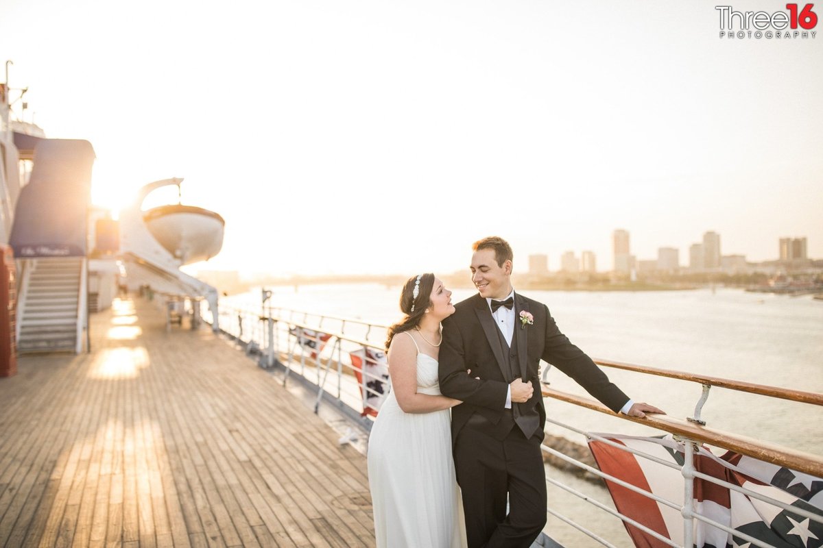 Bride cuddles up to her Groom as he smiles back at her while they are walking along the Queen Mary
