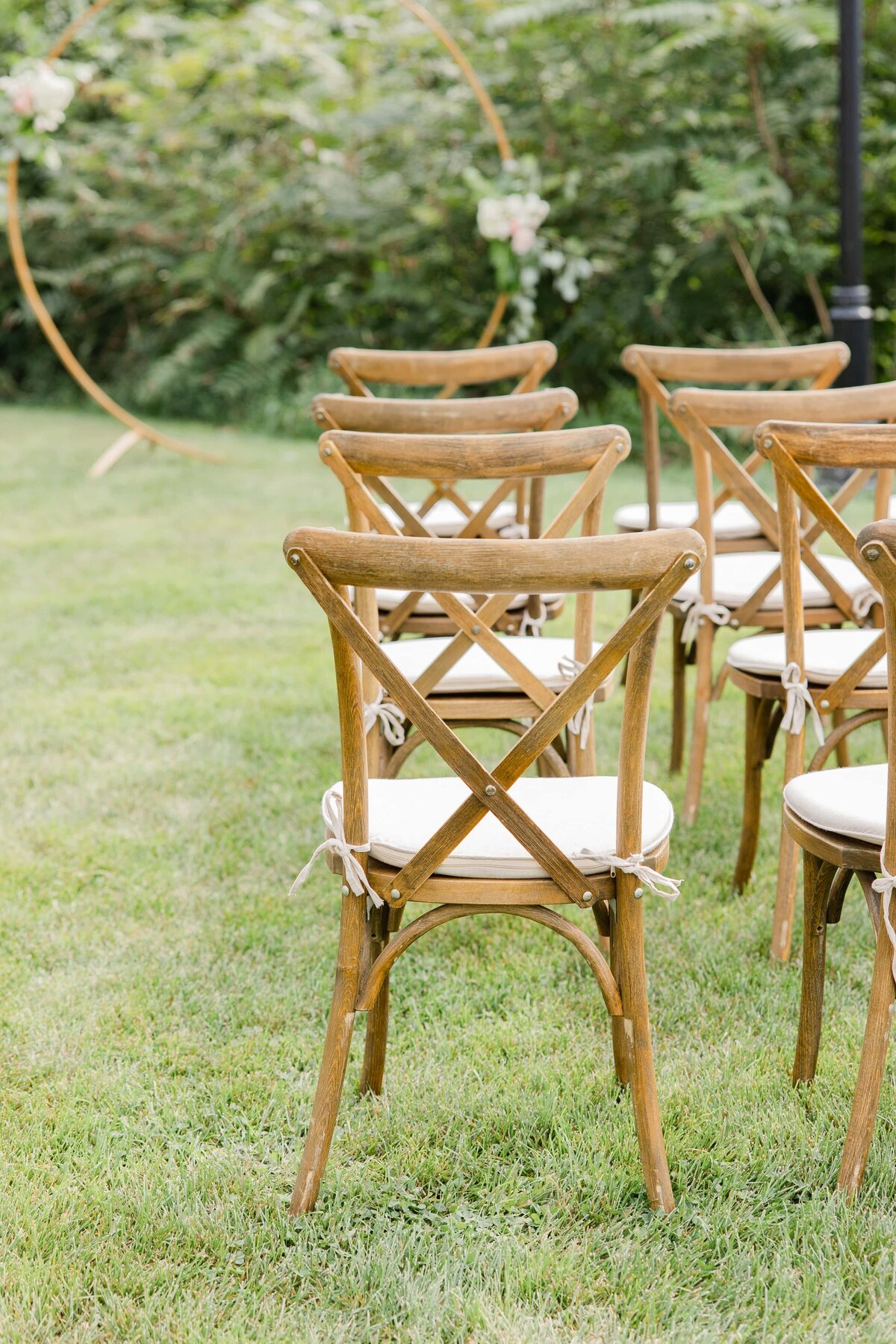 Wooden chairs with white cushions arranged on a lawn for an outdoor event in Iowa, with floral decorations visible in the background.