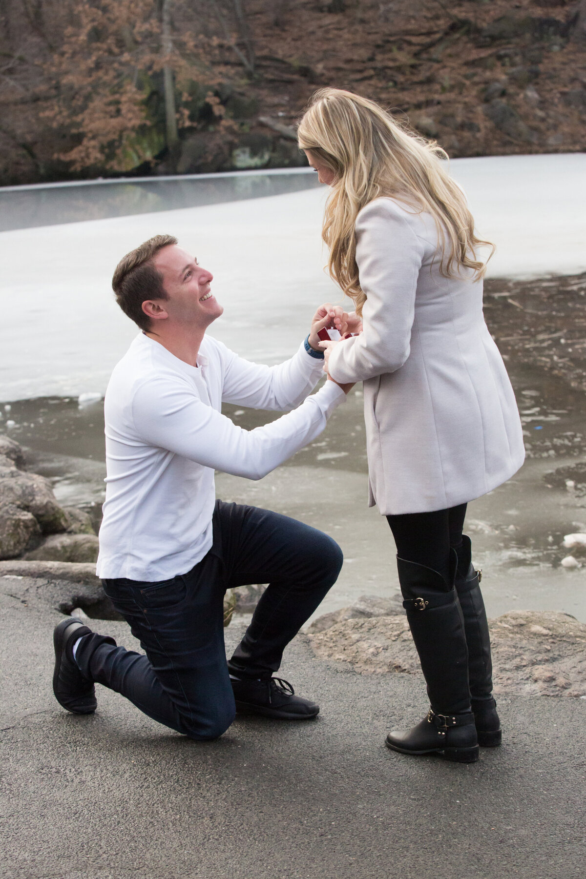 Man in white shirt proposes on one knee to girlfriend with blonde hair in Central Park engagement session New York wedding photographer